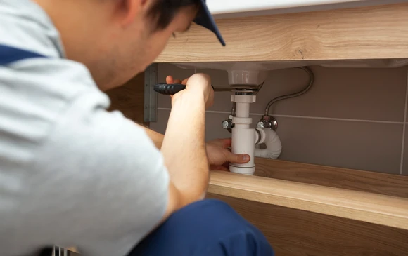 Plombier professionnel intervenant sous un &eacute;vier de cuisine, travaillant sur l'installation de plomberie