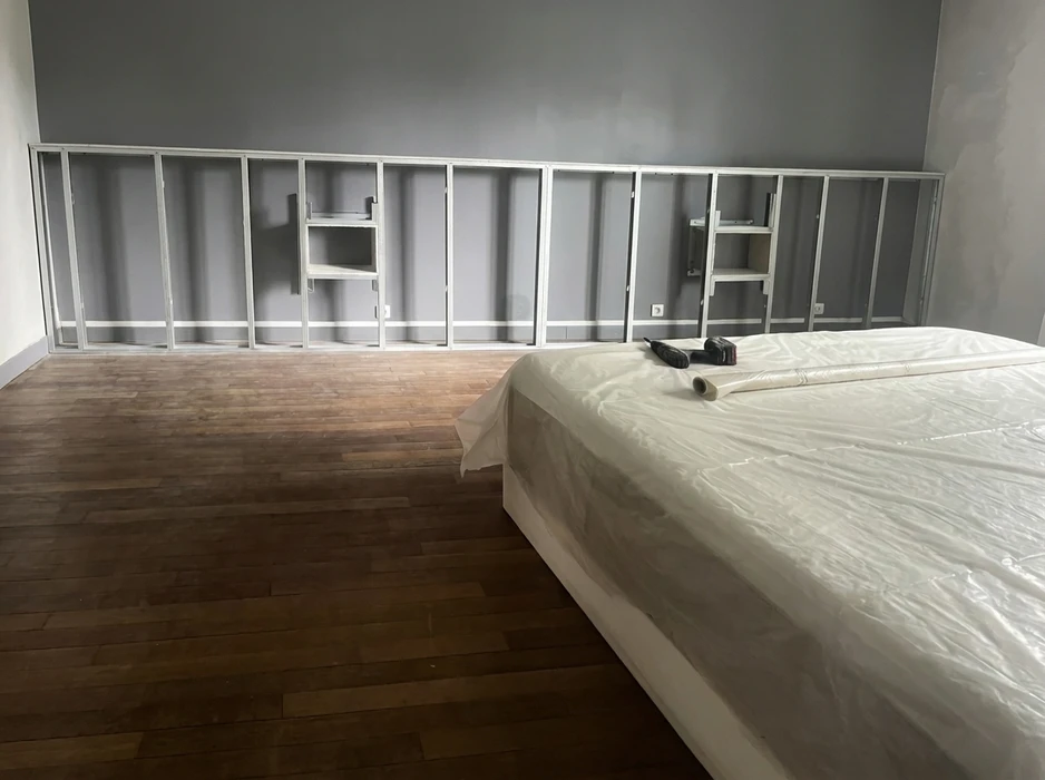 Chambre en cours de rénovation, sol en parquet massif foncé, mur peint en gris
