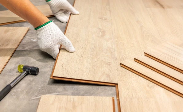 Pose de parquet flottant en int&eacute;rieur par un ouvrier portant des gants de protection blancs