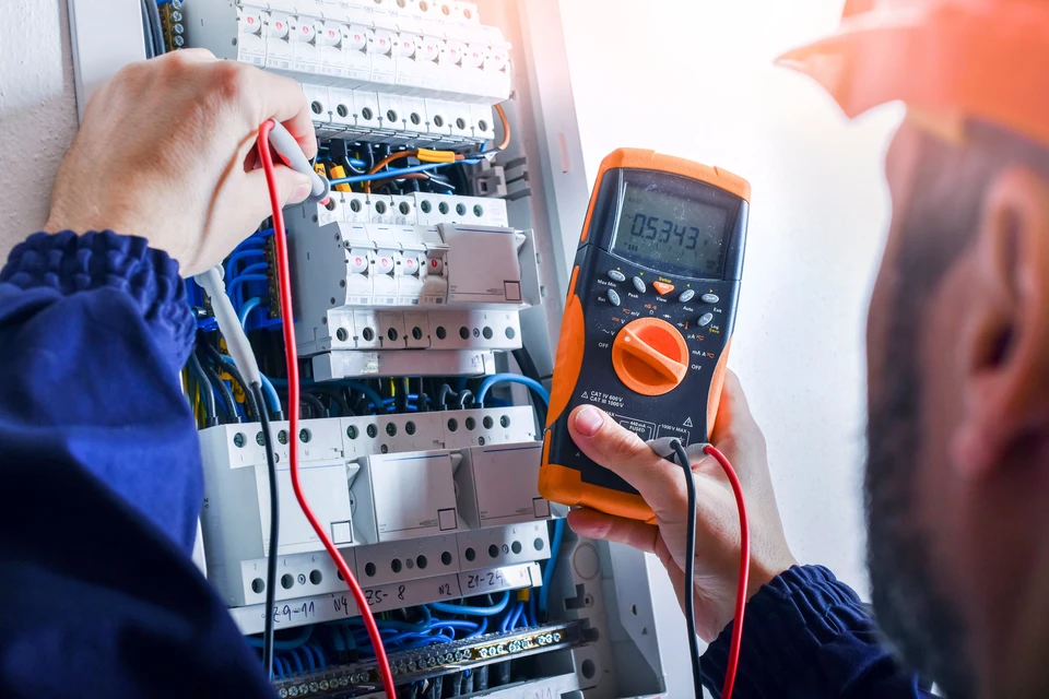 Électricien en combinaison bleue effectuant des mesures électriques dans un tableau de distribution ouvert