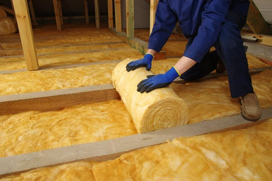 Artisan en tenue de travail et &eacute;quipement de protection installant de la laine min&eacute;rale ou de la mousse isolante sur la face int&eacute;rieure d'un mur existant d'une habitation, avec mise en &eacute;vidence des panneaux isolants positionn&eacute;s entre les montants de structure, dans un contexte de r&eacute;novation int&eacute;rieure r&eacute;sidentielle.