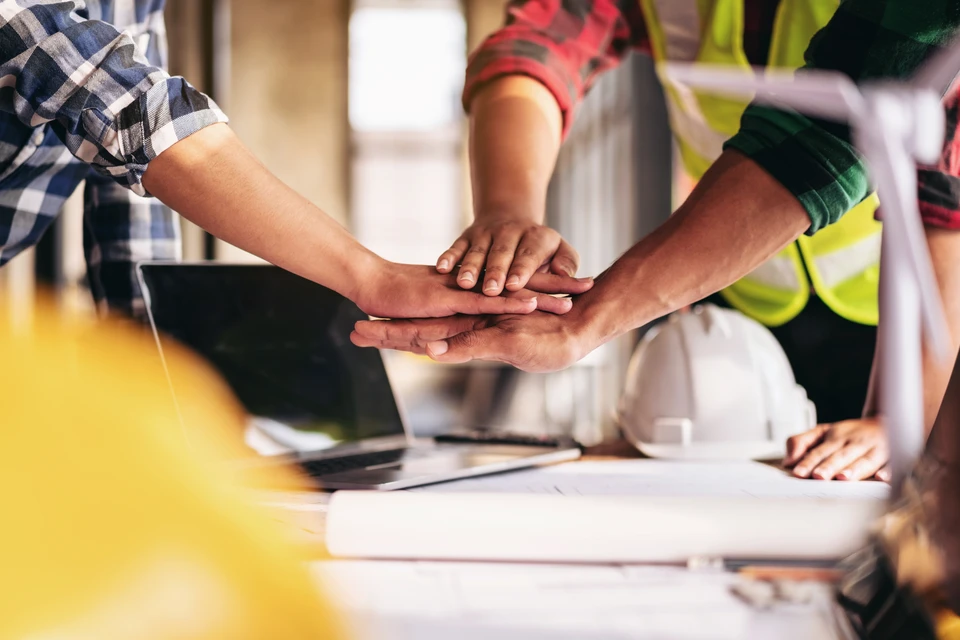 Scène de travail collaboratif en intérieur avec deux professionnels penchés sur des plans architecturaux étalés sur une table