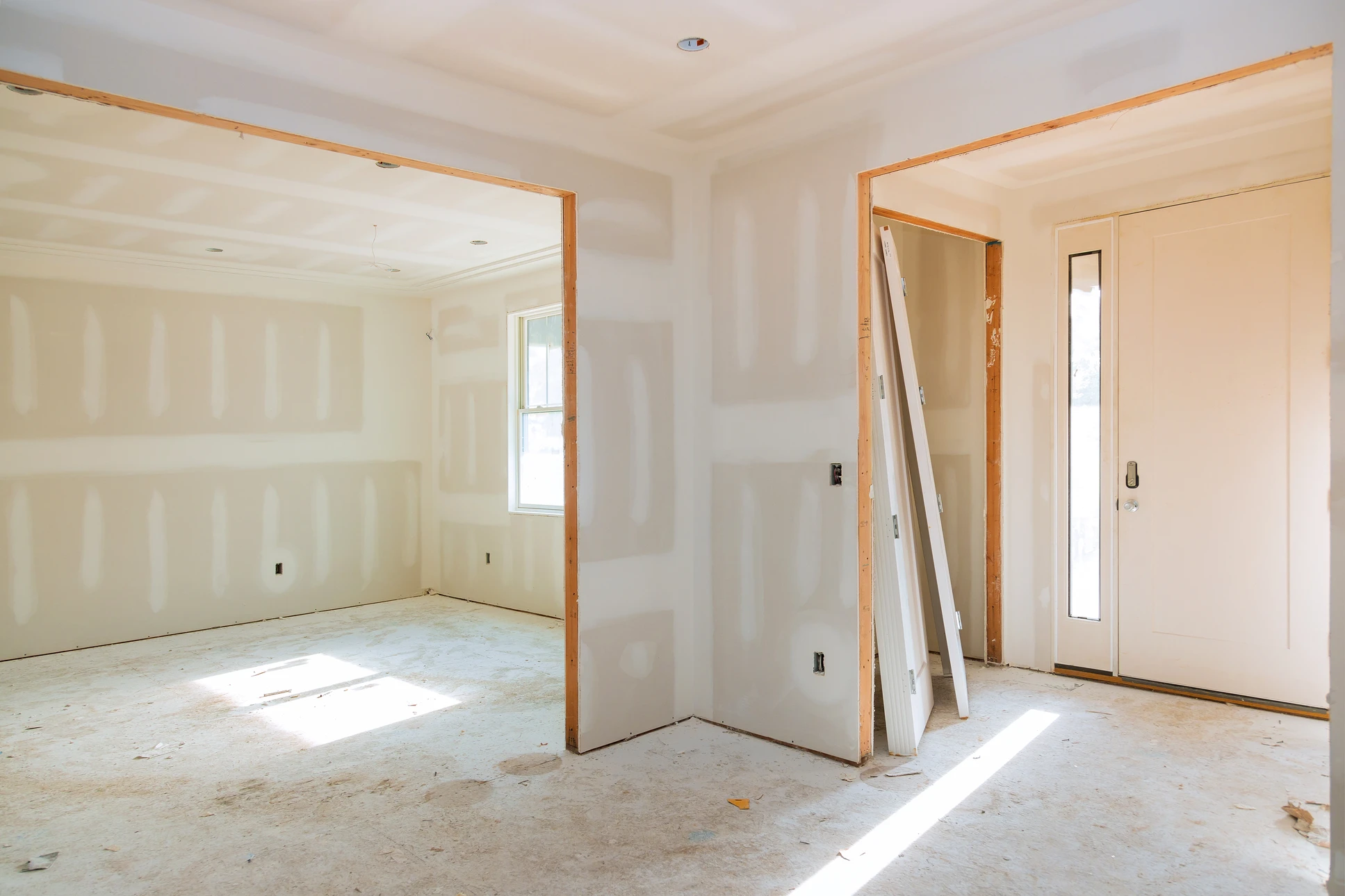 Ouvrier en bâtiment équipé d'un casque de sécurité jaune travaille à genoux sur un chantier intérieur, mesurant et positionnant des plaques de plâtre