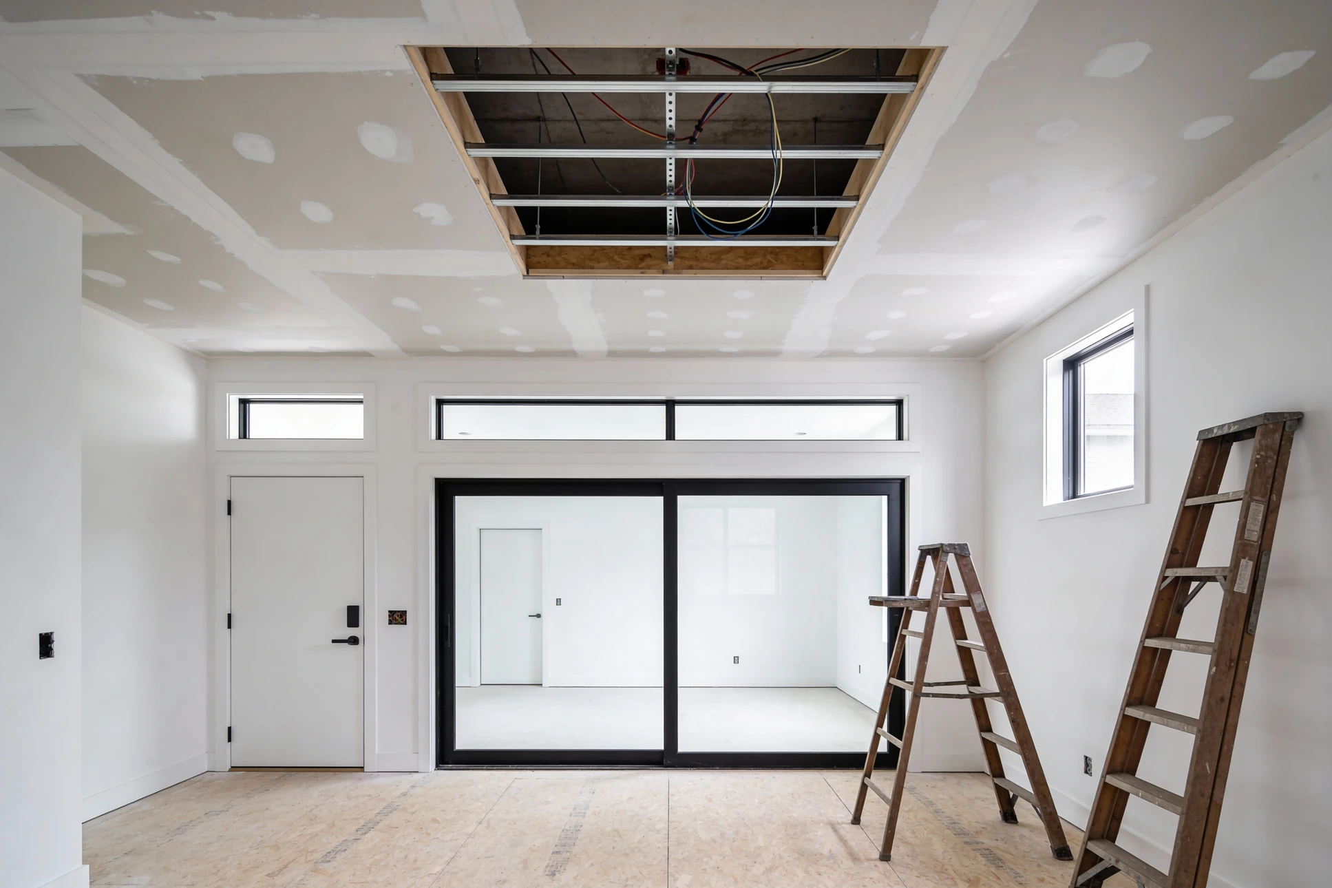 Ouvrier en bâtiment équipé d'un casque de sécurité jaune travaille à genoux sur un chantier intérieur, mesurant et positionnant des plaques de plâtre