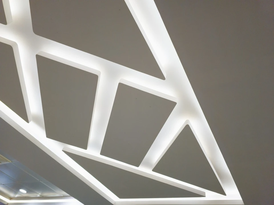 Un artisan installe un plafond suspendu dans un intérieur blanc